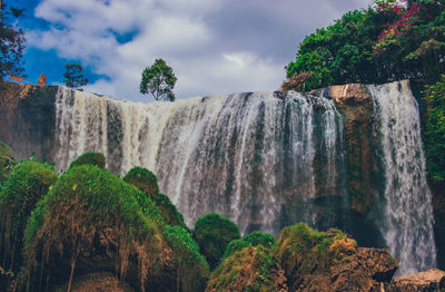 Low angle view of waterfall on cliff against sky