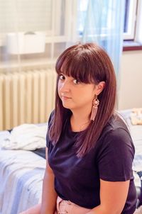 Portrait of young woman with bangs sitting on bed at home