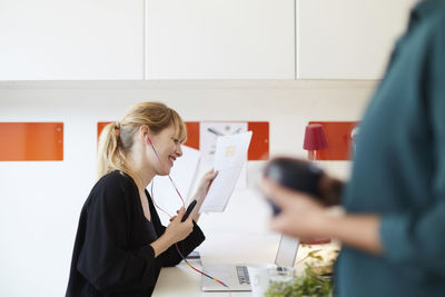 Smiling mid adult woman using hands-free device while holding document in office