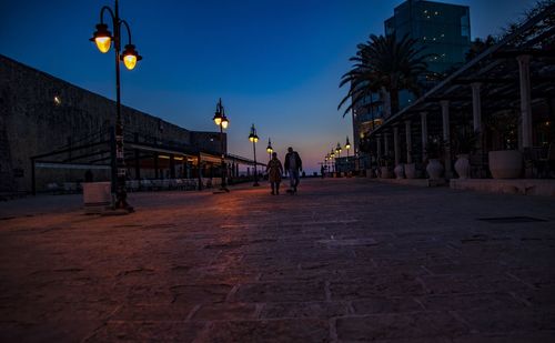 People walking on street amidst buildings in city at dusk