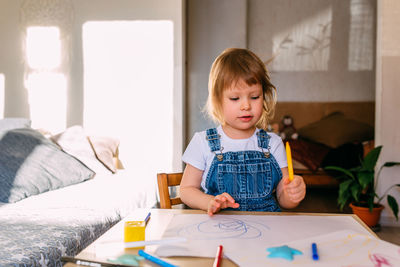 Small child at home at the children's table draws with felt-tip pens.