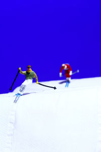 Low angle view of people skiing on snow against clear blue sky