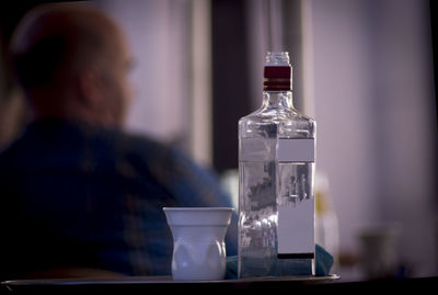 Reflection of man in glass bottle on table