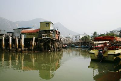 House over river by moored boats against sky