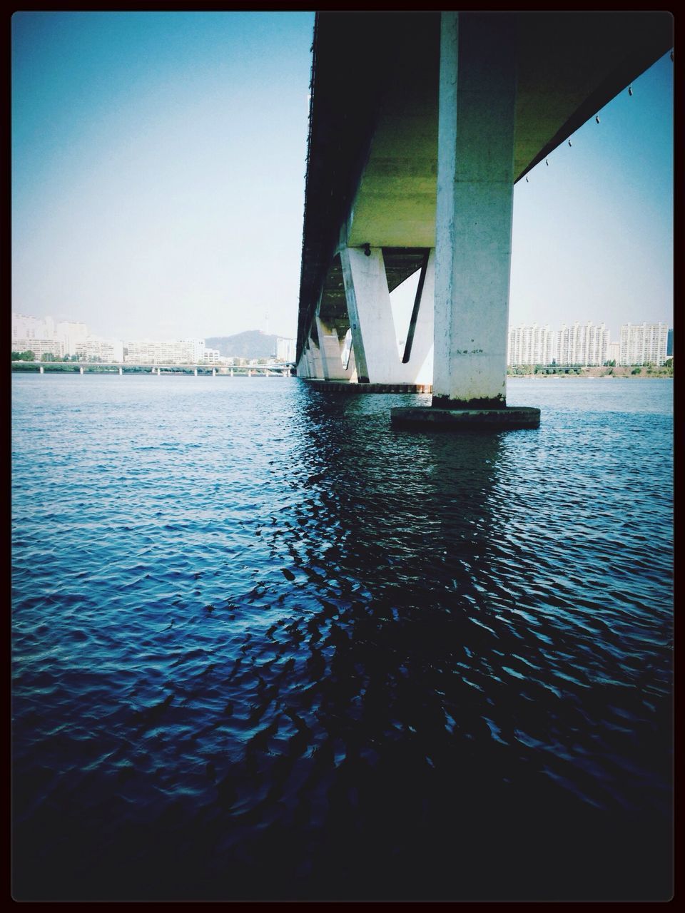 water, transfer print, transportation, nautical vessel, clear sky, auto post production filter, waterfront, sea, boat, rippled, built structure, mode of transport, river, architecture, reflection, connection, blue, bridge - man made structure, bridge, sunlight