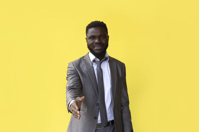 Portrait of young man standing against yellow background