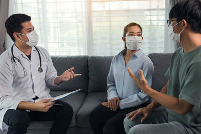Young couple wearing mask having discussion with doctor at home