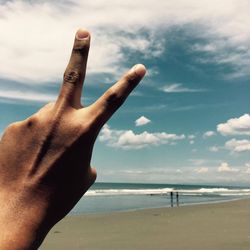 Close-up of hand on beach against sky