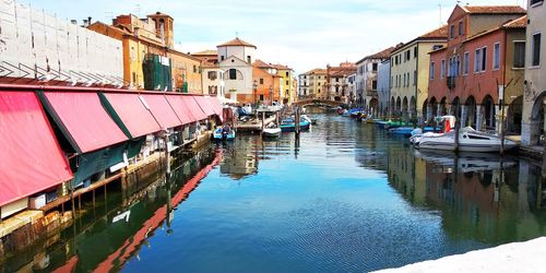 Boats moored in canal amidst buildings in city