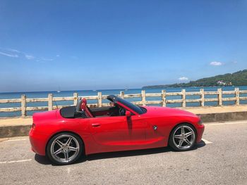 Red vintage car on road by sea against sky