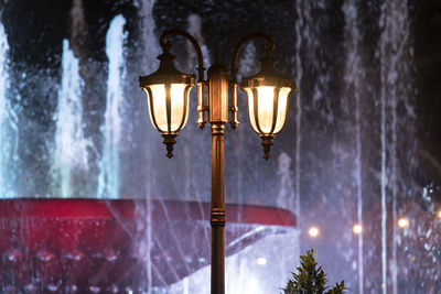 Low angle view of illuminated street lights against fountains in city at night