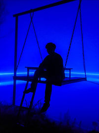 Rear view of silhouette man sitting on swing at playground