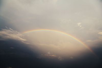 Rainbow over trees against cloudy sky