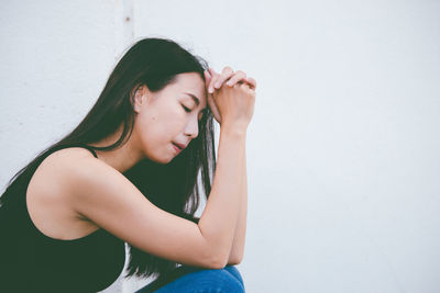 Beautiful young woman sitting against wall