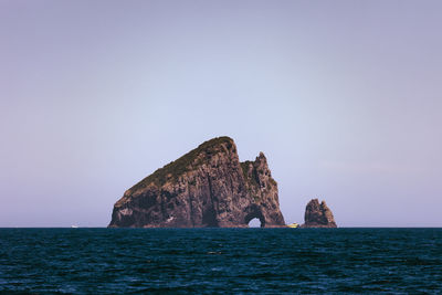 Rock formation in sea against clear sky