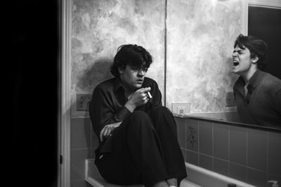 Multiple image of man smoking cigarette while shouting in bathroom in front of mirror