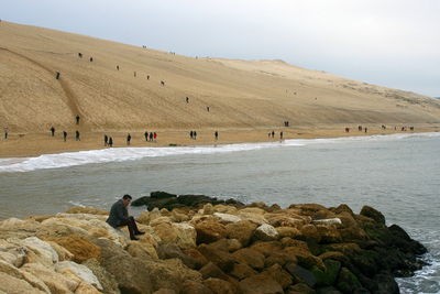 Man sitting on groyne by sea against sky