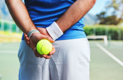 Midsection of man holding tennis ball standing on court