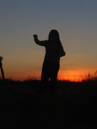 Silhouette man standing on field against sky during sunset