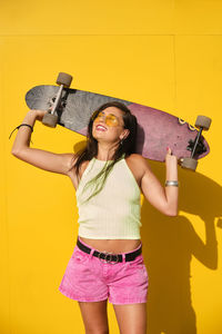 Portrait of beautiful young woman standing against yellow wall