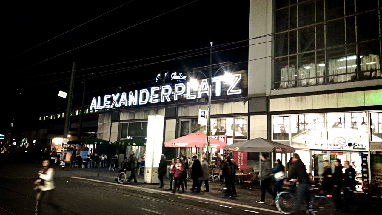 PEOPLE WALKING ON ILLUMINATED STREET IN CITY AT NIGHT