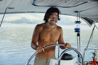 Happy shirtless man looking away while sailing boat on sea