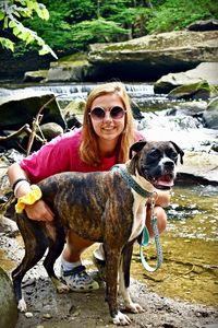 Portrait of smiling young woman with dog at riverbank