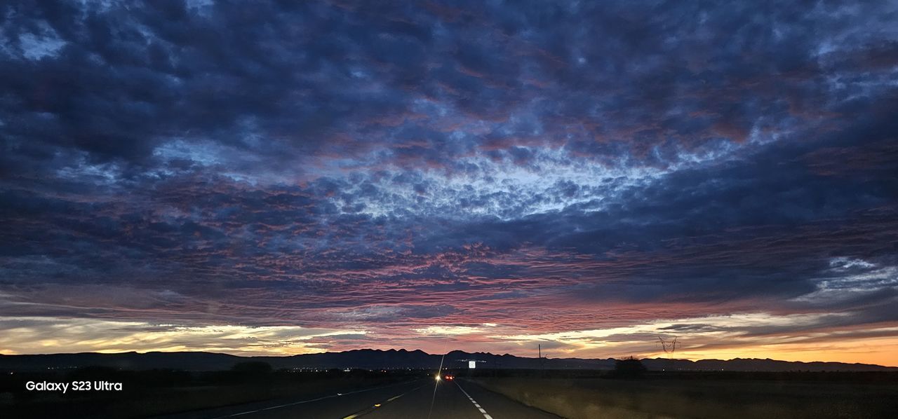 sky, cloud, road, transportation, sunset, horizon, nature, sign, dramatic sky, highway, dusk, environment, landscape, the way forward, beauty in nature, evening, no people, scenics - nature, symbol, mode of transportation, night, street, city, travel, outdoors, motor vehicle, vanishing point, car, cloudscape, motion, road marking, marking, long exposure, afterglow, storm, travel destinations