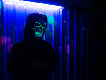 Serial killer wearing neon skull mask at halloween costume party with colorful background.