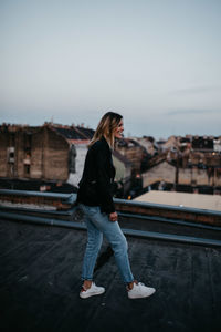 Smiling young woman walking against cityscape during sunset