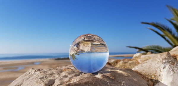 Close-up of crystal ball on rocks by sea against clear blue sky