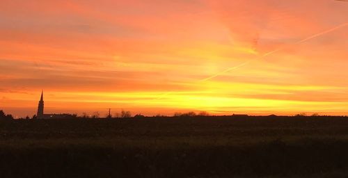 Scenic view of silhouette field against orange sky