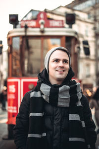 Smiling young man looking away against tram in city during winter