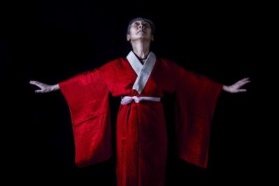 Young man with arms raised standing against black background