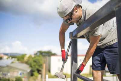 Construction worker using hammer to build steel railing on roof.