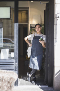 Portrait of a smiling young woman standing at entrance of building