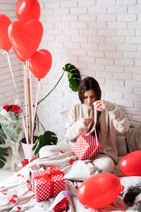 Young caucasian brunette woman sitting in the bed celebrating valentine day wrapping the gifts