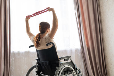 Rear view of woman exercising on wheelchair at home