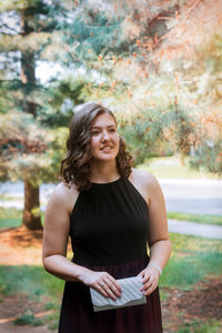 Teenage girl looking away while standing against trees