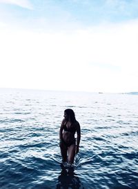 Full length of shirtless young woman in sea against sky