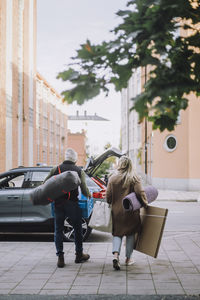 Rear view of mature couple with luggage walking towards car