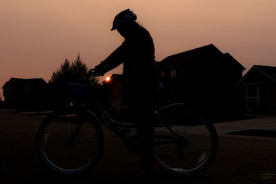 Silhouette man riding bicycle against sky at sunset