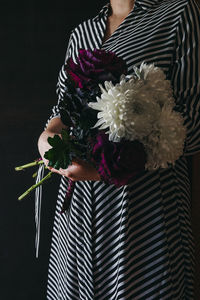 Midsection of woman holding bouquet against black background