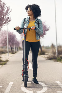 Woman looking away while standing with electric push scooter on road