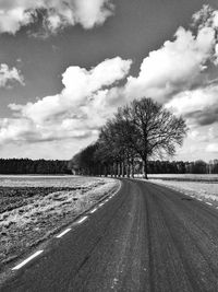 Road passing through field against cloudy sky