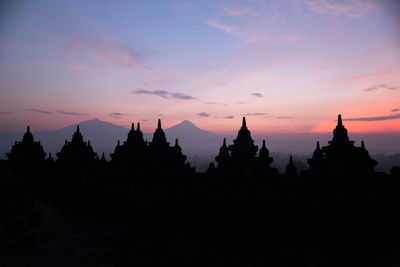 Silhouette temple against buildings during sunset