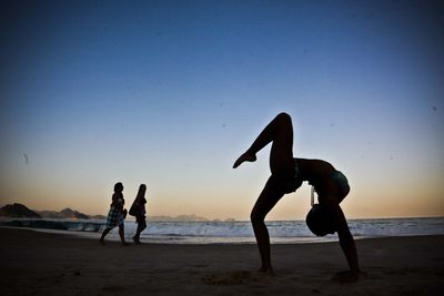 Silhouette people on beach against clear sky during sunset