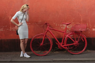 Young woman laughing while standing by red bicycle against wall