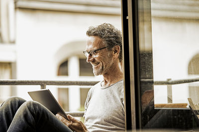 Smiling man sitting on balcony using digital tablet