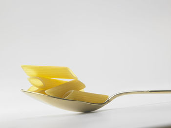 Close-up of raw pasta on spoon against white background